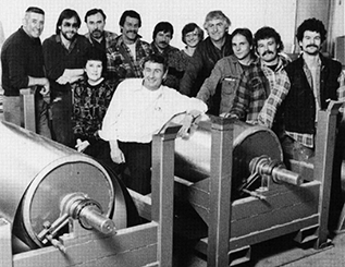 A black and white image of twelve Modern Niagara employees posed around rolls of sheet metal.