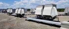 Multiple Air Handling units in rows on the roof of a building, connected by numerous ducts, with a cloudy blue sky in the background.